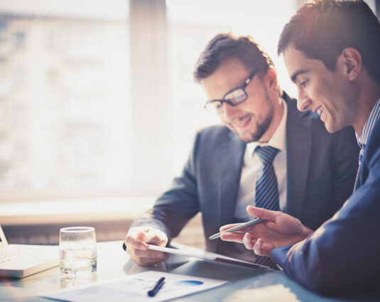 Image of two young businessmen using touchpad at meeting